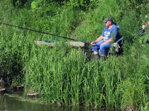 Mężczyzna łowi ryby nad turkusowym jeziorem w Koninie, otoczony bujną zielenią.