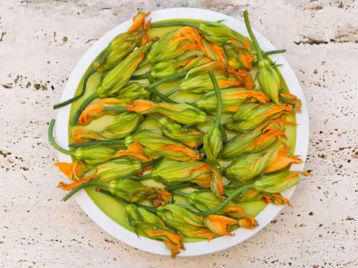 Fiori di zucca freschi, pronti per essere cucinati in padella, su un piatto bianco.