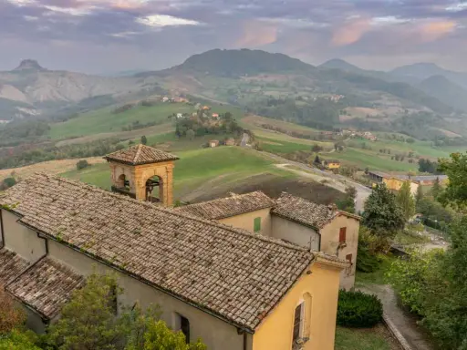 Borghi collinari perfetti per gite in giornata da Reggio Emilia. Un campanile svetta tra tetti antichi e dolci pendii verdi.