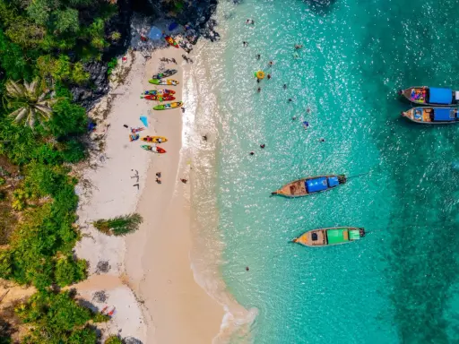 Rajska plaża na tajlandzkiej wyspie Phuket. Kajaki czekają na plaży, a turyści kąpią się w turkusowej wodzie.