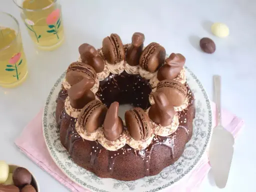Gâteau rond au chocolat, décoré de macarons, de lapins en chocolat et d'une ganache carambar onctueuse.