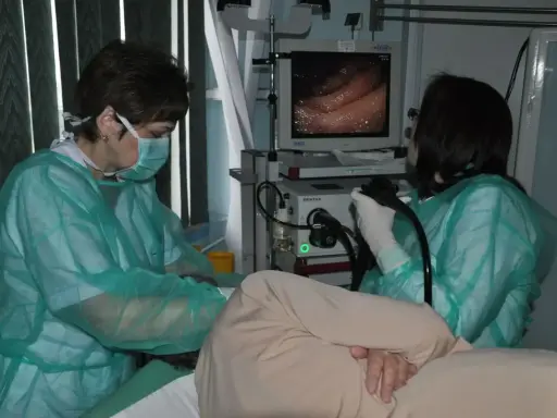 Lekarze w zielonych fartuchach wykonują gastroskopię, obserwując obraz z wnętrza żołądka na monitorze.