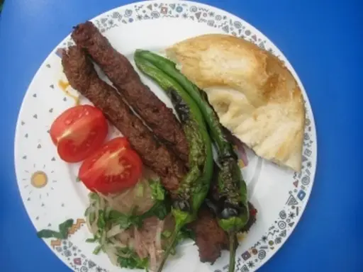 Adana Kebap mit gegrillten Peperoni, Tomaten und Fladenbrot auf einem Teller.