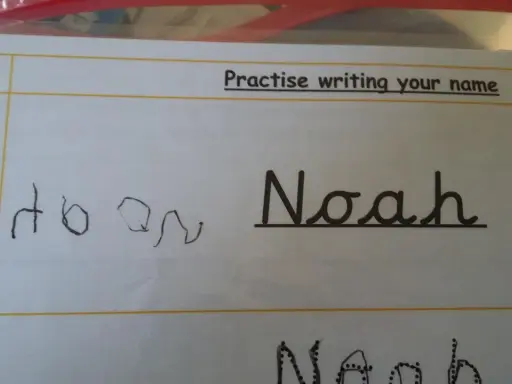 Siedmiolatek ćwiczy pisanie imienia "Noah" w lustrzanym odbiciu. Obok widać próbę pisania imienia.