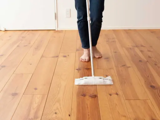 Persona descalza limpiando parquet con una mopa. El suelo de madera luce brillante y cuidado.