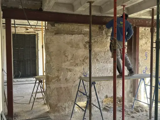 Trabajador realiza el empresillado de pilares en una obra. Se aprecian puntales metálicos y vigas de soporte.