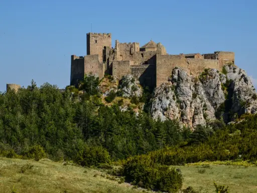 Das Castillo de Loarre thront majestätisch auf einem Felsen, umgeben von grünen Wäldern und unter blauem Himmel.