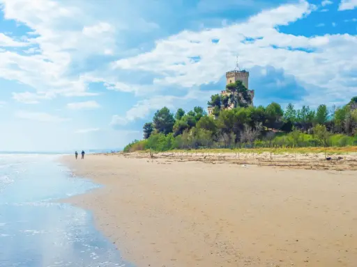 Passeggiata sulla spiaggia di Pineto mare, con un castello in lontananza tra i pini.
