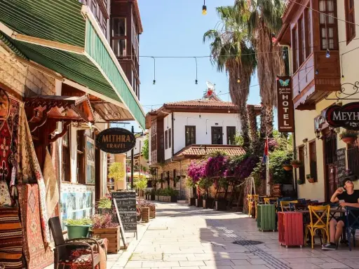 Bunte Gassen in der antalya altstadt mit Teppichläden, Palmen und einem Café, wo ein Mann entspannt sitzt.