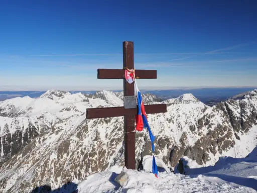 Drewniany krzyż z flagą Słowacji na szczycie Kriváň, narodowej góry Słowaków, na tle ośnieżonych Tatr.