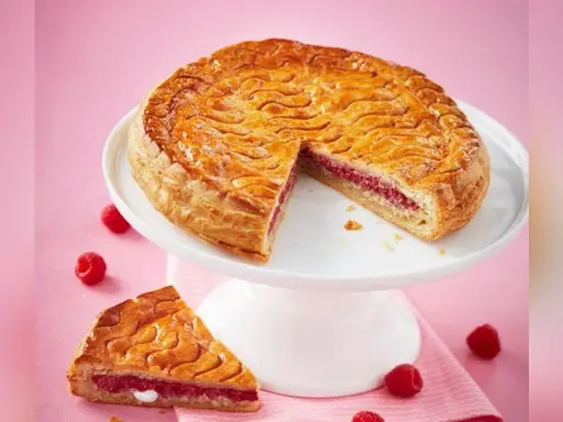Galette framboise dorée sur un présentoir blanc, une part coupée révèle la garniture rose. Parfait pour une recette galette framboise.