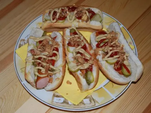 Cztery pyszne domowe hot dogi z kiełbaską, ogórkiem, ketchupem, musztardą i chrupiącą cebulką na talerzu.