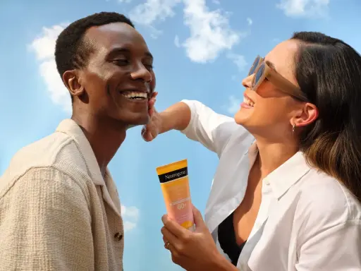 Un homme rit sous le soleil, une femme lui applique de la crème solaire pour protéger son visage.