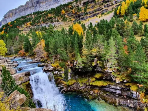 Cascada en un bosque otoñal de la cola de caballo huesca, con aguas turquesas y rocas cubiertas de musgo.