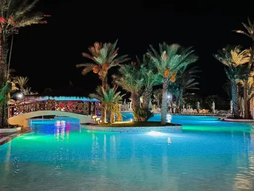 Nocny basen z palmami i mostkiem, idealne miejsce na relaks. Wiele pozytywnych fiesta beach djerba opinie potwierdza jego urok.
