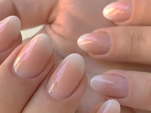Delikatne, owalne paznokcie z subtelnym, perłowym połyskiem. Klasyczny francuski manicure w nowoczesnym wydaniu, podkreślający naturalne piękno dłoni.