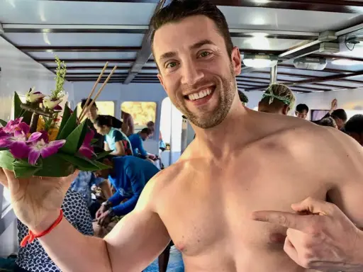 Smiling man on a boat in Asia, holding a flower offering. A perfect moment for gay travel in Asia.