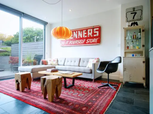 En röd persisk matta ger inspiration till detta vardagsrum med grå soffa, träpallar och en vintage-skylt.
