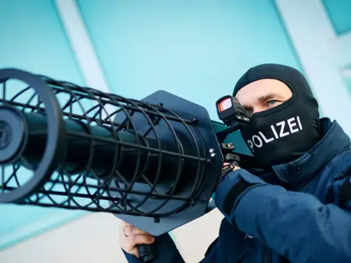 Polizist mit Sturmhaube und "POLIZEI"-Aufdruck zielt mit einer Drohnenabwehrwaffe.