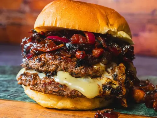 Saftiger Burger mit doppeltem Patty, geschmolzenem Käse und einer süß-salzigen Bacon Jam-Schicht, garniert mit roten Zwiebeln.