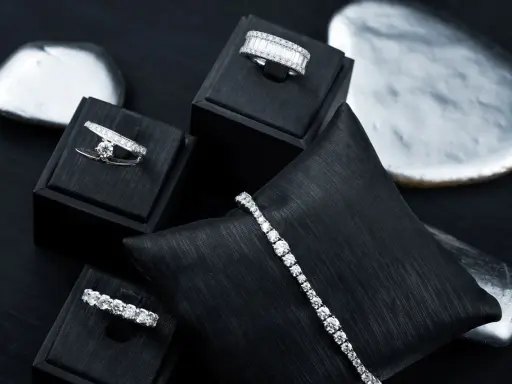 Gioielli scintillanti, anelli e bracciali con diamanti, esposti su supporti neri e pietre levigate.