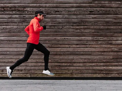 Ein Mann im roten Shirt und schwarzer Hose absolviert einen kraftvollen crescendo lauf vor einer rustikalen Holzfassade.