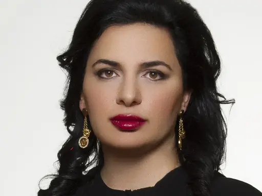 Portret Ruja Ignatova, kobiety o ciemnych włosach i wyrazistych ustach, w złotych kolczykach.