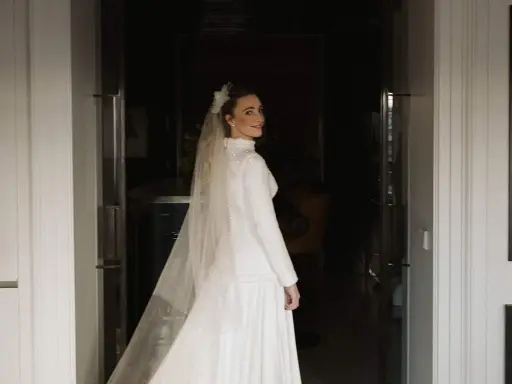 Novia sonriente con velo y vestido blanco, parte de un ajuar de novia tradicional, lista para su gran día.