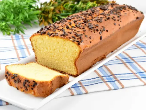 Puszysta babka z adwokatem, posypana czekoladową posypką, na białej paterze. Obok leży kromka ciasta.