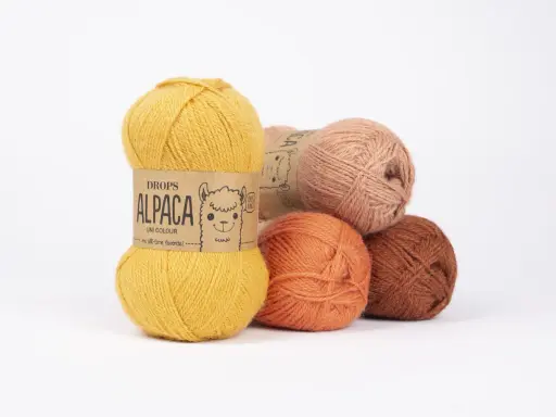Garnnystan i varma färger som ockra, orange och rost. En guldig nystan från Drops Alpaca har en söt alpacka på etiketten.