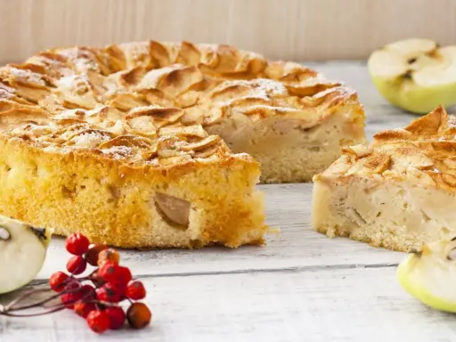 Un gâteau compote de pomme sans sucre, saupoudré de sucre glace, avec des quartiers de pomme et des baies rouges sur une table en bois.