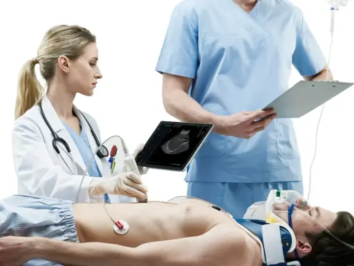 Lekarka wykonuje USG pacjenta, który leży na stole. Obok stoi lekarz z notatkami. Szybka diagnostyka to klucz do ratowania życia.