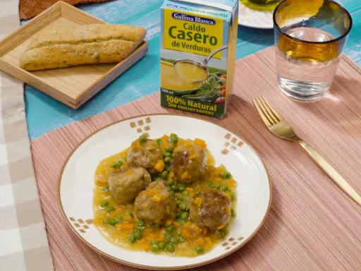Albondigas a la jardinera en salsa con guisantes y zanahoria, acompañadas de pan y caldo de verduras.