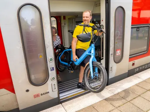 Mann mit blauem E-Bike steigt in den Zug. Perfekt, um das E-Bike im Zug mitzunehmen und die Reise fortzusetzen.
