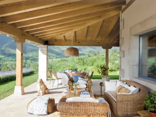 Ideas para como decorar porche de entrada: muebles de mimbre, mesa de comedor, un perro y vistas espectaculares.
