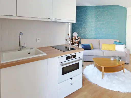 Aménagement petite cuisine moderne avec évier, plaque induction, four et salon cosy avec canapé bleu et jaune.