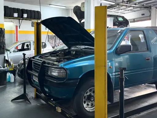 Taller mecánico con coches en reparación. Un todoterreno azul tiene el capó abierto, y se pregunta qué significa elevalunas.