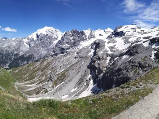 Panoramica mozzafiato dei fotografi sui tornanti dello Stelvio, con vette innevate e un cielo azzurro intenso.