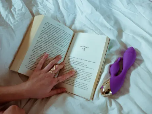 Kobieta czyta książki erotyczno romantyczne, a obok leży fioletowy wibrator.
