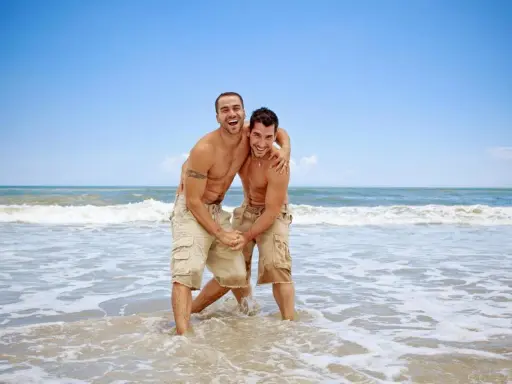 Two men laughing and embracing in the shallow waves of the Torremolinos gay beach.