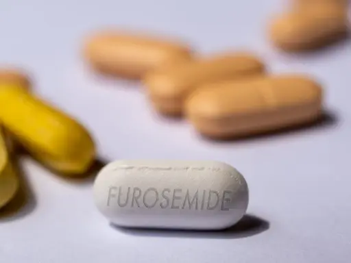 Biała tabletka z napisem FUROSEMIDE na pierwszym planie, otoczona innymi tabletkami w kolorze żółtym i beżowym.