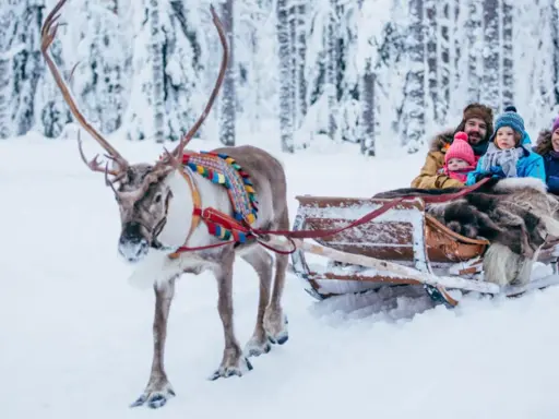 Familie im Rentierschlitten im verschneiten Wald, ein magischer Ausflug im Weihnachtsmann-Dorf Finnland.