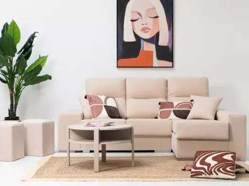 Sofá modular beige con chaise longue a la derecha, mesa auxiliar redonda, alfombra de yute, plantas y cuadro abstracto.