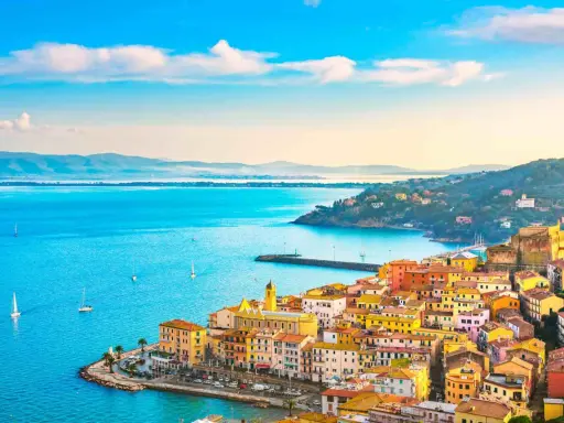 Colorate case affacciate sui mari della Toscana, con barche a vela che solcano le acque azzurre sotto un cielo limpido.