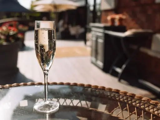 Ein Glas Sekt auf einem Tisch im Freien. Auch wenn Sekt kein Verfallsdatum hat, sollte er frisch genossen werden.