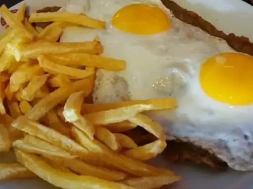 Un plato de milanesa a caballo argentina con papas fritas doradas y dos huevos fritos con yemas perfectas.