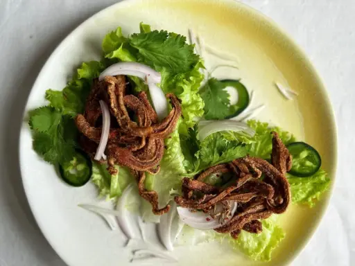 Crujiente oreja de cerdo frita servida sobre lechuga con cebolla morada, cilantro y jalapeño.