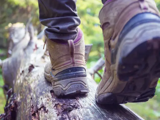 Na leśnej ścieżce, po powalonym pniu, idzie osoba w butach trekkingowych. Czy buty trekkingowe powinny być większe? Zapewne tak, by zapewnić komfort podczas długich wędrówek.
