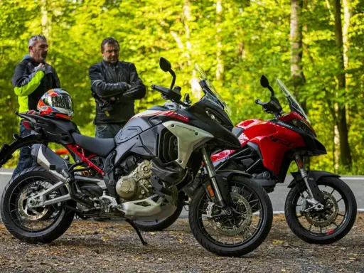Dwóch motocyklistów przy dwóch motocyklach Ducati Multistrada V2, jeden szary, drugi czerwony, na tle leśnej drogi.