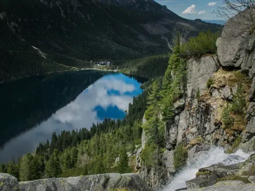 Gdzie jest Morskie Oko? Jezioro odbija chmury, otoczone lasem i górami. Wodospad spada po skalnej ścianie.